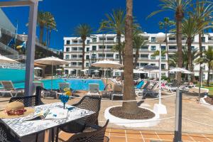 a resort with a pool with tables and chairs and palm trees at Alsol Walhalla in Playa del Ingles