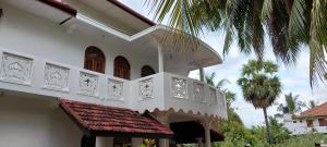 a white building with a balcony and a palm tree at Shiven Homestay in Kallady
