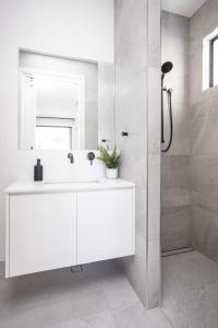La salle de bains blanche est pourvue d'un lavabo et d'une douche. dans l'établissement Sailfish Studio - Beachside Private Access Granny Flat by uHoliday, à Kingscliff
