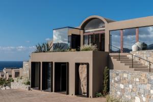 a large house with glass doors and a stone wall at Acro Suites - A Wellbeing Resort in Agia Pelagia