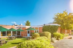 a brick building with picnic tables and green umbrellas at Holiday Inn Basingstoke, an IHG Hotel in Basingstoke