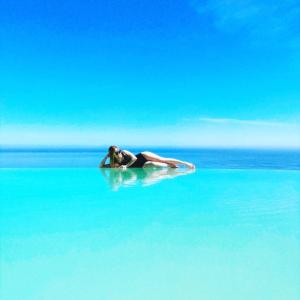 a woman laying on a surfboard in the water at Hotel Antica Cascina Del Golfo in Scopello