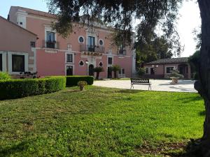 a park with a bench in front of a pink building at Hotel Lady Lusya in Siracusa