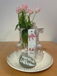 talerz z dwoma kieliszkami do wina i wazon z różowymi kwiatami w obiekcie Ferienapartment Alex am See w mieście Friedrichshafen