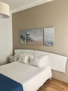 a bedroom with a white bed with three paintings on the wall at Arcada House Tavira in Tavira