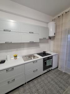 una cocina con armarios blancos, fregadero y alfombra en Best View Residence, en Costinesti