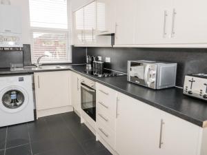 a kitchen with white cabinets and a washer and dryer at 10 Carmen Sylva Road in Llandudno