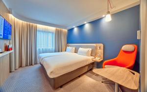 ロンドンにあるホリデイ イン エクスプレス ロンドン ストラトフォードのベッドと赤い椅子が備わるホテルルームです。