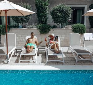 a man and a woman sitting on a lawn chair under an umbrella at Hotel Harmony by Aycon in Petrovac na Moru