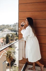 a woman in a white shirt and black pants drinking a glass of water at Hotel Lusso Mare by Aycon in Budva