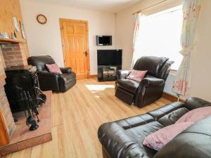 sala de estar con muebles de cuero y chimenea en Carnmore Cottage, en Dungloe