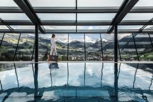 kobieta z walizką stojącą przed basenem w obiekcie Lebenberg Schlosshotel-Kitzbühel w mieście Kitzbühel