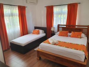 two beds in a room with orange curtains and windows at Grace Self Catering in Anse aux Pins