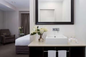 a bathroom with a sink and a bed with a mirror at Rydges Auckland in Auckland