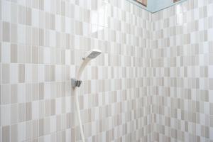a white tiled bathroom with a shower head on a wall at RedDoorz near Yogyakarta International Airport in Glagah