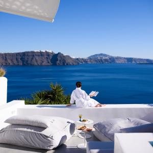 a person sitting on a couch reading a book overlooking the water at Lathouri Cave Villa in Oia