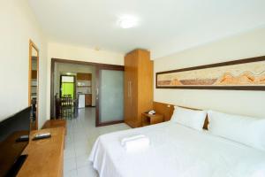 a bedroom with a white bed and a kitchen at Araça Flat Natal Prime - Beira Mar in Natal