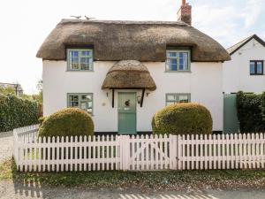 a thatched cottage with a white picket fence at Thatchings in Bude