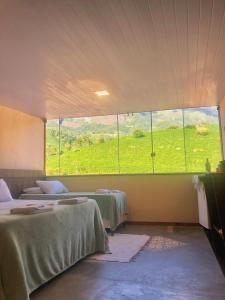 two beds in a room with a large window at Estalagem e Restaurante Cantinho Bistrô in Alto Caparao
