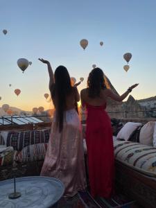 dos mujeres de pie en una azotea mirando globos de aire caliente en Rose Cave Hotel en Göreme