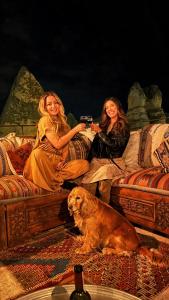 dos mujeres sentadas en una cama con un perro en Rose Cave Hotel en Göreme