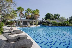 a swimming pool with chaise lounge chairs and palm trees at Villa Bima II in Nusa Dua