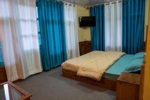 a bedroom with a bed with blue curtains and a tv at The Vagabond Manali in Manāli