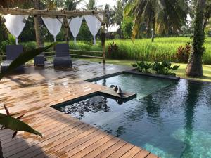 a pool with two chairs and a wooden deck at Villa WHITE KAROUNA in Sukawati