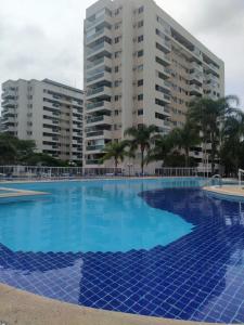 a large blue swimming pool with buildings in the background at Lindo apto Recreio RJ, em frente ao Rio Centro in Rio de Janeiro
