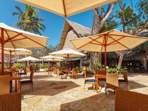 a patio with tables and chairs with umbrellas at Safari Beach Hotel in Diani Beach