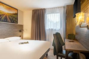 ein Hotelzimmer mit einem weißen Bett, einem Schreibtisch und einem Fenster in der Unterkunft The Originals City, Angers Sud, Le Village 49 in Les Ponts-de-Cé