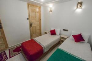 a bedroom with two beds with red pillows and a door at Dar Zin in Fez