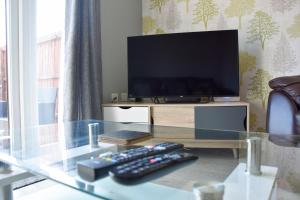 a glass table with a tv and two remote controls at Queens Lodge - Beautiful Modern House with Free Parking - Marvello Properties in Norwich