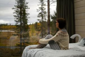 a woman sitting on a bed looking out a window at Iisakki Village in Ruka