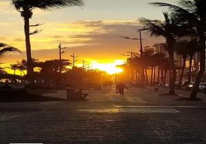 une personne marchant dans une rue avec le coucher du soleil en arrière-plan dans l'établissement Kitpraiana Ocean, à Praia Grande