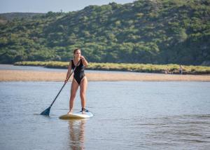 a woman standing on a paddle board in the water at Hotel Vale Da Telha in Aljezur