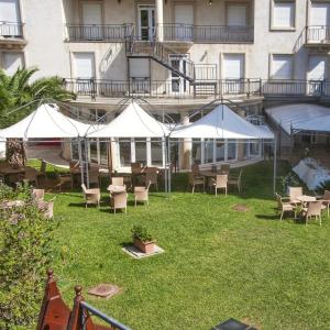 um pátio com mesas, cadeiras e guarda-sóis brancos em Mariano IV Palace Hotel em Oristano