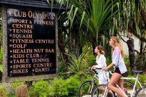 two women riding bikes in front of a sign at The Warwick Fiji in Korolevu