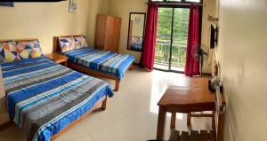 1 dormitorio con 2 camas, mesa y ventana en North 27 Hill Transient Rooms near Microtel Inn and Victory Liner Baguio en Baguio