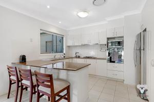 a kitchen with white cabinets and a bar with chairs at KOZYGURU | Westleigh | Spacious Home with 4 Beds in Thornleigh