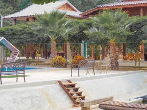 a pool with benches and palm trees in front of a building at บ้านสวนเปรมณัฐตรา in Ban Song (1)