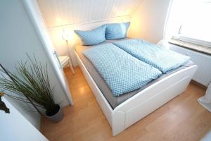 ein weißes Bett mit blauen Kissen und einer Pflanze in einem Zimmer in der Unterkunft Ferienwohnung Langeoog in Neuharlingersiel