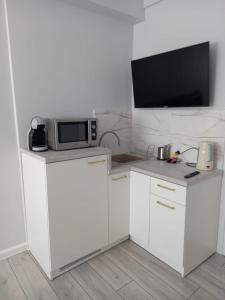 a kitchen with white cabinets and a tv on a wall at Rewianka Apartamenty przy samej plaży in Rewa