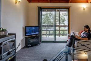 un uomo seduto su una sedia in un soggiorno che guarda la tv di Freycinet Cottage 1 – Bluestone a Coles Bay