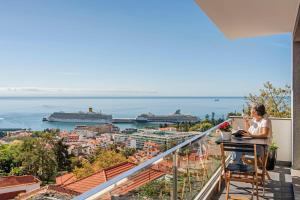 a woman sitting at a table on a balcony looking at the ocean at Casa do Castelo by An Island Apart in Funchal