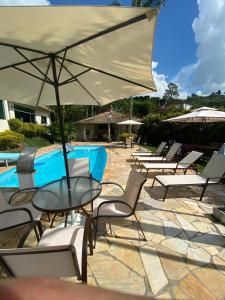 a table and chairs with an umbrella next to a pool at Casa de campo, com quadra de Beach Tennis, Volei e Fut Volei próxima a SP!! in Santana de Parnaíba