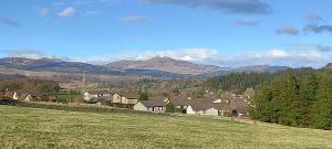 a village with a green field and mountains in the background at CORSBIE VILLA GUEST HOUSE in Newton Stewart