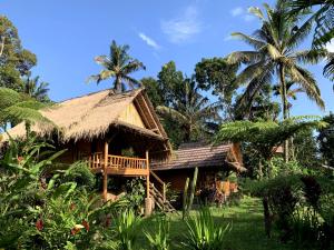 a house with a thatched roof and palm trees at Tetebatu Sama Sama Bungalows in Tetebatu