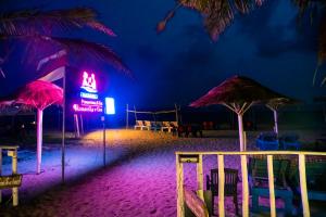 a beach with umbrellas and a neon sign at night at Village Susegat Beach Resort in Morjim