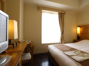 a hotel room with a bed and a desk with a television at Hotel Monterey Lasoeur Ginza in Tokyo